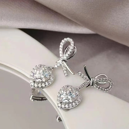 LUMIOR Amour Solitaire 2 karaat hartvormige moissanite oorbellen met strikdetail en platina plating.