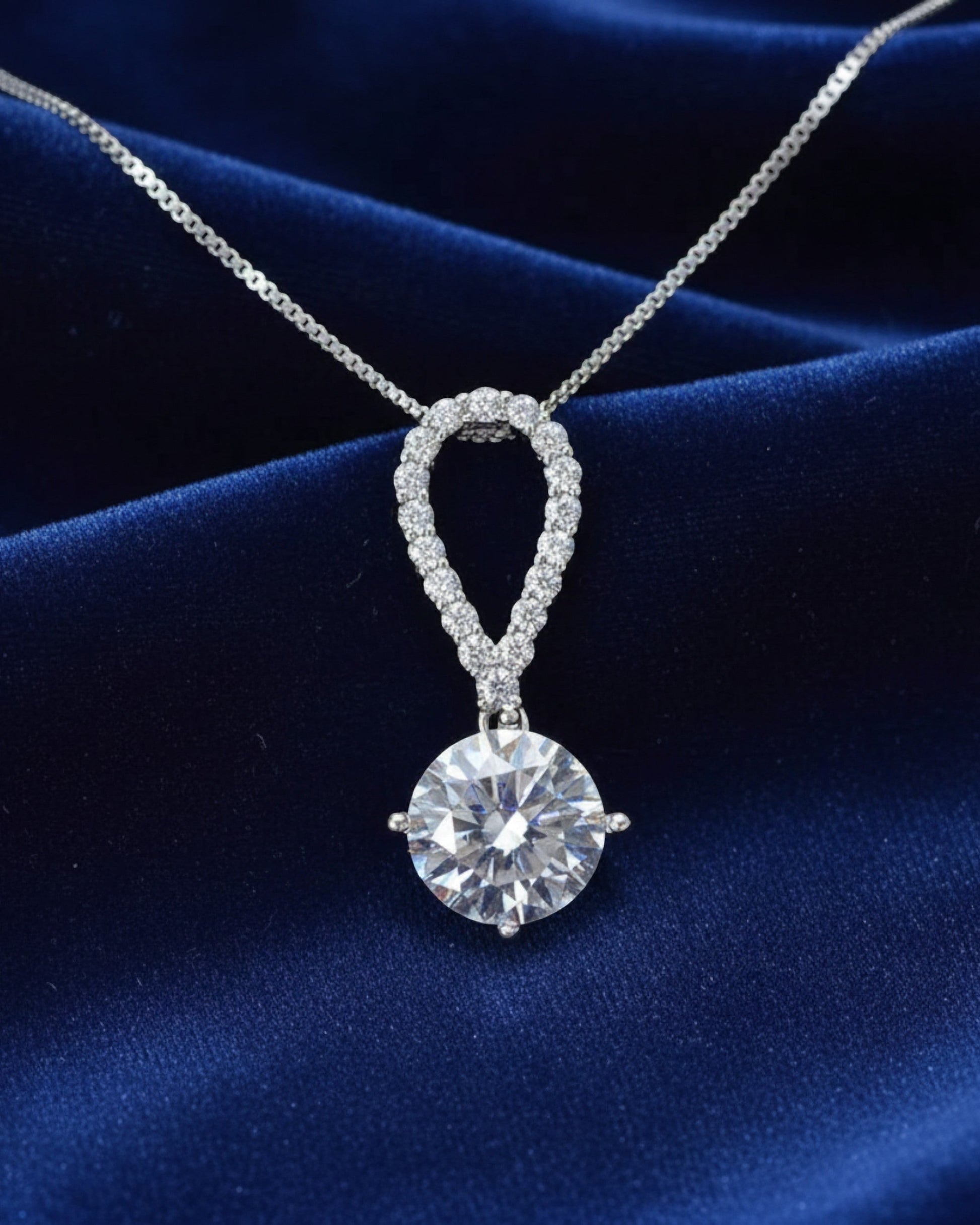 LUMIOR 5 karaat moissanite ketting met peervormige hanger in 925 sterling zilver op een blauwe fluwelen achtergrond.